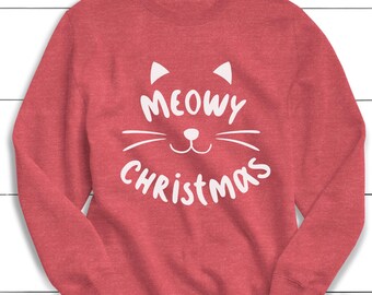 Peut inclure: Sweat-shirt rouge à manches longues avec un motif de visage de chat blanc et le texte "MEOWY CHRISTMAS".