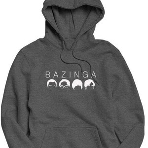 May include: A dark grey hooded sweatshirt with the word "BAZINGA" printed in white on the front. Five white silhouettes of people's heads are printed below the word.
