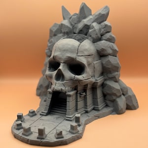 May include: A 3D printed miniature of a skull-shaped temple with a stone entrance and a pathway leading to it. The temple is surrounded by rocks and crystals.