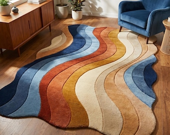 Op de afbeelding: Een vloerkleed met een onregelmatige, organische vorm met een reeks golvende, parallelle banen in een kleurverloop van diep marineblauw, lichtblauw, gebrand oranje, mosterdgeel en crème, met een getextureerd, pluizig oppervlak.