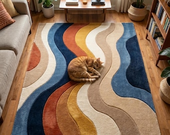 Op de afbeelding: Een rechthoekig vloerkleed met een herhalend patroon van golvende, verticale strepen in marineblauw, roestoranje, mosterdgeel, crème en beige. Een oranje cyperse kat ligt opgerold in het midden van het kleed op de houten vloer.