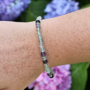 May include: A green, purple, and black beaded bracelet with a stretchy elastic band.