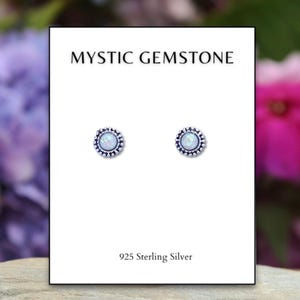 May include: A pair of silver stud earrings with a white opal gemstone in the center of each earring. The earrings are surrounded by a silver beaded border. The card reads "Mystic Gemstone" and "925 Sterling Silver".