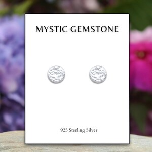May include: A pair of silver stud earrings with a hammered texture. The earrings are on a white card with the text "Mystic Gemstone" and "925 Sterling Silver".
