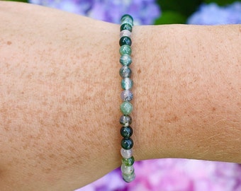 May include: A green, gray, and white agate beaded bracelet. The bracelet is made of small, round beads and is worn on a person's wrist.