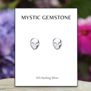 May include: A pair of silver alien head stud earrings on a white card with the text "MYSTIC GEMSTONE" and "925 Sterling Silver".