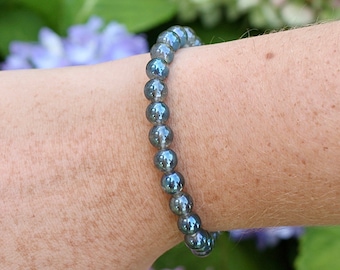 May include: A beaded bracelet made of iridescent blue labradorite stones. The bracelet is on a person's wrist.