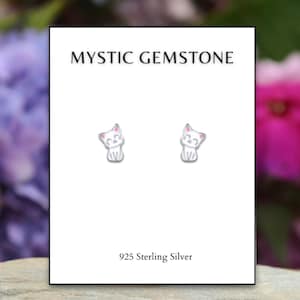 May include: A pair of sterling silver cat stud earrings on a white card. The earrings are small, with a smiling cat design and pink accents. The card reads "MYSTIC GEMSTONE" and "925 Sterling Silver".