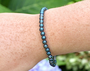 May include: A dark blue beaded bracelet with iridescent shimmer. The bracelet is made of small, round beads and is worn on a person's wrist.