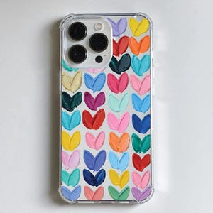 May include: Clear phone case with a colorful heart design. The case features a pattern of painted hearts in various colors, including red, orange, yellow, green, blue, purple, and pink. The phone's camera lenses are visible.