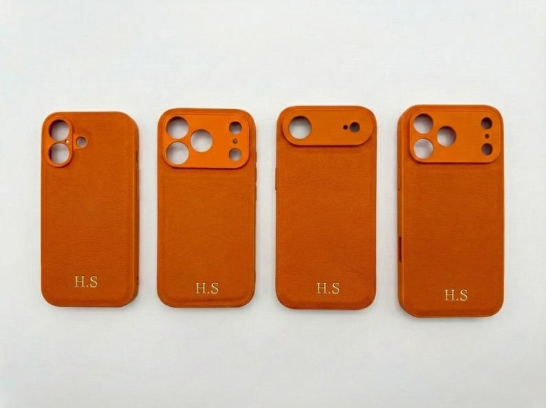 K&ouml;nnte beinhalten: Vier orangefarbene Handyh&uuml;llen mit unterschiedlichen Kameraausschnitten. Jede H&uuml;lle hat die Initialen "H.S." unten. Die H&uuml;llen bestehen aus einem strukturierten Material und sind auf wei&szlig;em Grund angeordnet.