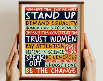 May include: A framed print with a motivational message in colorful text. The message reads "Now more than ever we must stand up, demand equality, honor our differences, defend the constitution, trust women, pay attention, read real news, believe in science, be generous, speak out, help those in need, choose love, be the change."