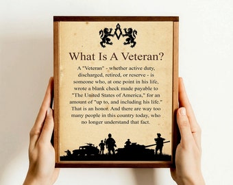 Op de afbeelding: Een ingelijst afdruk met een bruine houten lijst en een beige achtergrond. De afdruk toont een zwart silhouet van soldaten en een tank met de tekst "What Is A Veteran?" en een definitie van het woord "Veteran".