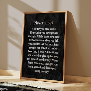 May include: A black and white inspirational quote poster with the text "Never forget" and a message about perseverance and strength. The poster is framed in a wooden frame.