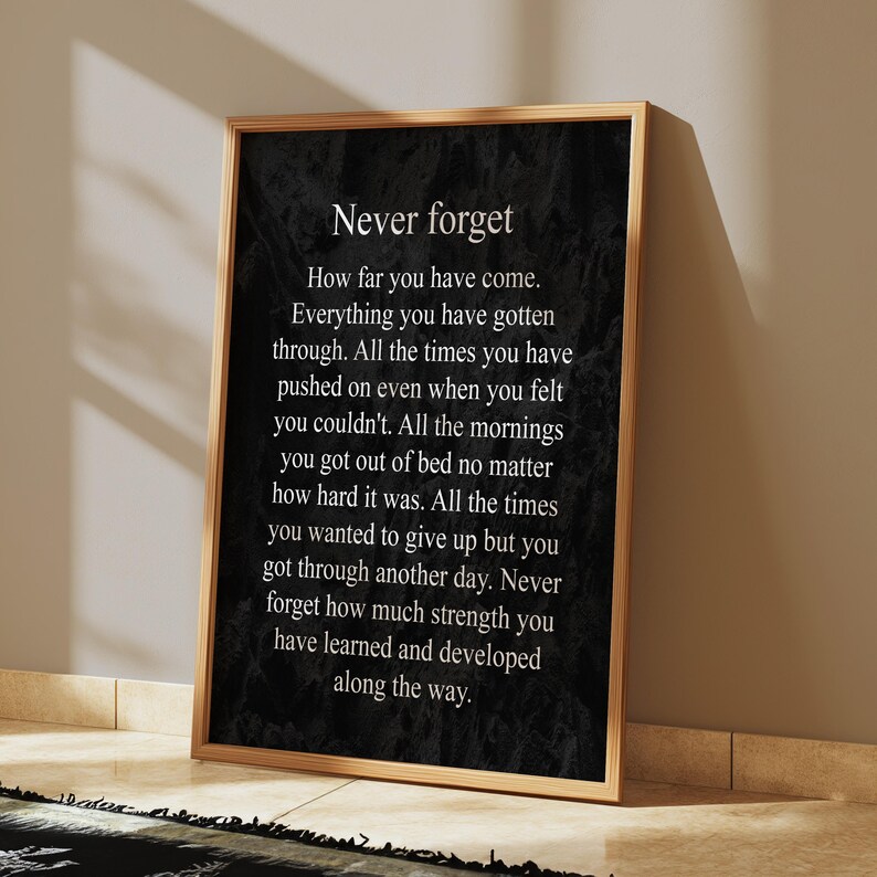 May include: A black and white inspirational quote poster with the text "Never forget" and a message about perseverance and strength. The poster is framed in a wooden frame.