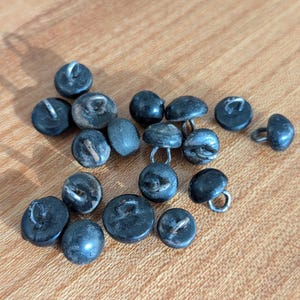 May include: A collection of 17 black plastic buttons with metal loops. The buttons are round and have a smooth finish.