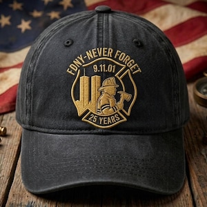 Puede incluir: Una gorra de béisbol negra con bordado dorado de un emblema de bombero, las Torres Gemelas y el texto FDNY-NEVER FORGET 9.11.01 25 YEARS. La gorra tiene una corona estructurada, una visera curva y un botón en la parte superior del diseño.