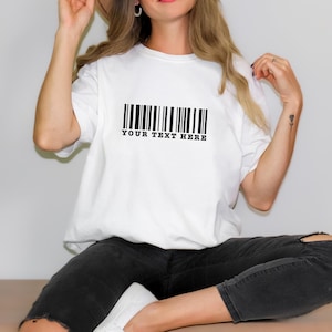 Peut inclure: T-shirt blanc avec un graphique de code-barres noir et le texte "YOUR TEXT HERE" imprimé en dessous.
