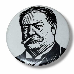 May include: A circular pinback button featuring a high-contrast black and white graphic illustration of a man with a prominent mustache and formal attire. The design uses bold lines and shading to depict the facial features and clothing.