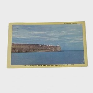May include: Vintage postcard featuring Split Rock Lighthouse on Lake Superior, Minnesota. The image shows the lighthouse atop a cliff, with a forest and the lake under a cloudy sky. The postcard has a yellow border.