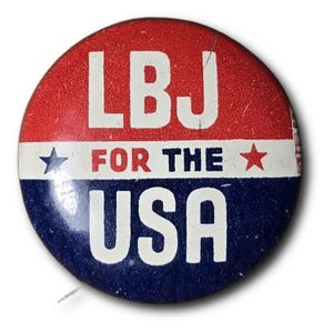 May include: A circular political campaign button featuring a red top section with the white text LBJ, a white middle stripe with the red text FOR THE, and a blue bottom section with the white text USA. Two small stars flank the central text.