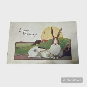 Könnte beinhalten: Vintage Ostergrußkarte mit einer idyllischen Szene mit zwei Hasen. Einer ist weiß mit blauen Flecken, der andere braun und weiß. Die Karte trägt die Aufschrift "Easter Greetings".