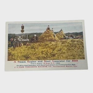 May include: Vintage postcard featuring a steam engine and steel separator in a field. The image shows a steam engine with several people and a large haystack. Text on the card reads "A Steam Engine and Steel Separator".