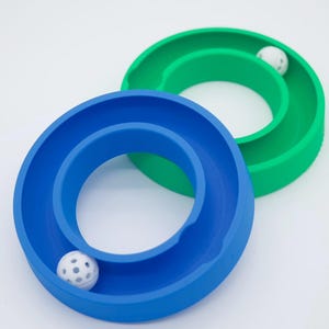 May include: Two plastic rings, one blue and one green, with a white ball in each. The rings are designed to be used as a toy for rolling the balls around.