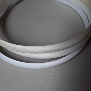 May include: Three white satin headbands, stacked on top of each other. The headbands are all the same size and shape, and they are made of a soft, silky material.