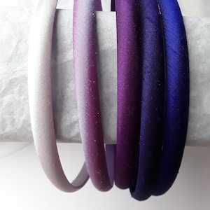 May include: Five satin headbands in shades of purple and blue. The headbands are arranged in a gradient from light to dark.