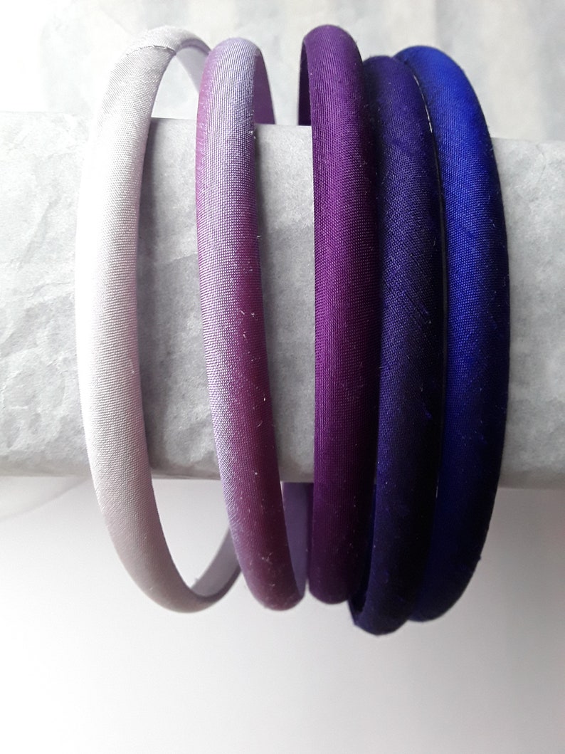 May include: Five satin headbands in shades of purple and blue. The headbands are arranged in a gradient from light to dark.