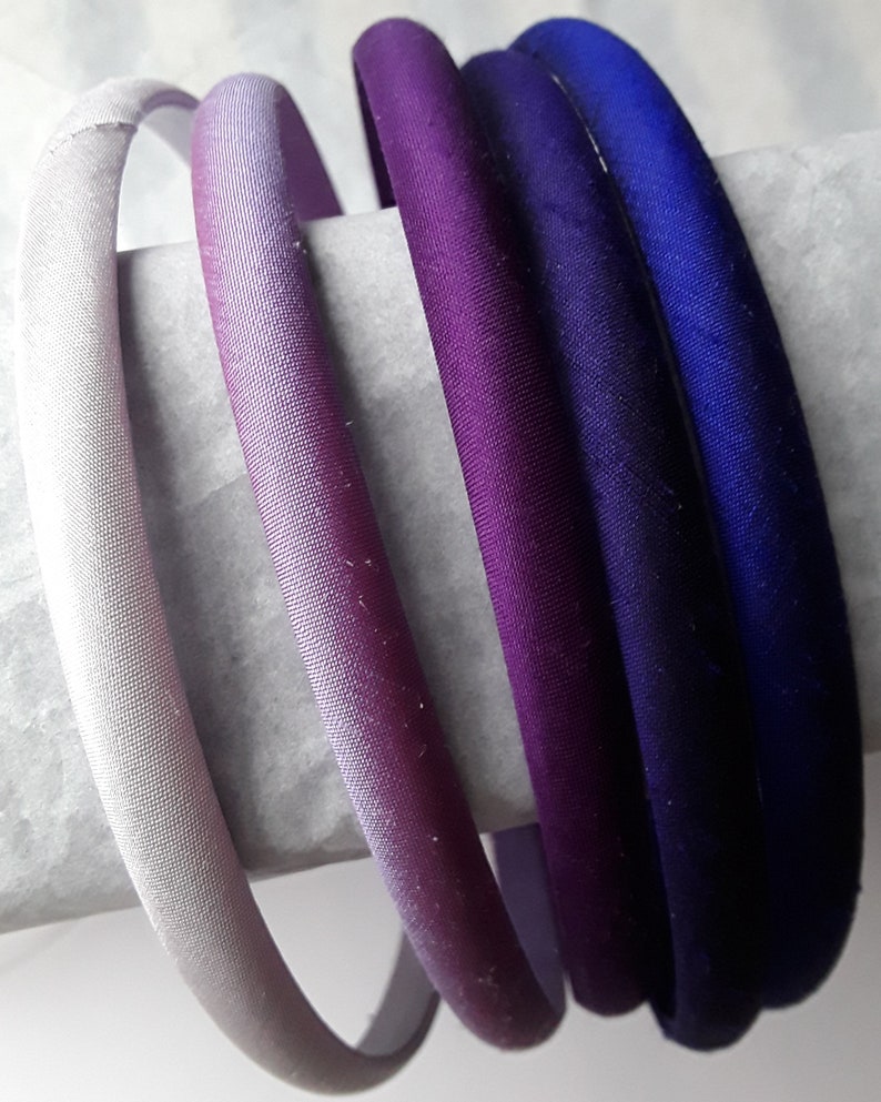 May include: Five fabric headbands in shades of purple, blue, and white. The headbands are ombre, with the color fading from dark to light.