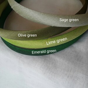 May include: Four different shades of green fabric headbands. The headbands are arranged in a circle, with the lightest shade of green at the top and the darkest shade of green at the bottom. The shades of green are sage green, olive green, lime green, and emerald green.