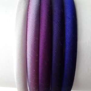 May include: Set of six hair ties in a gradient of colors from white to purple to blue. The hair ties are made of a soft, silky fabric.