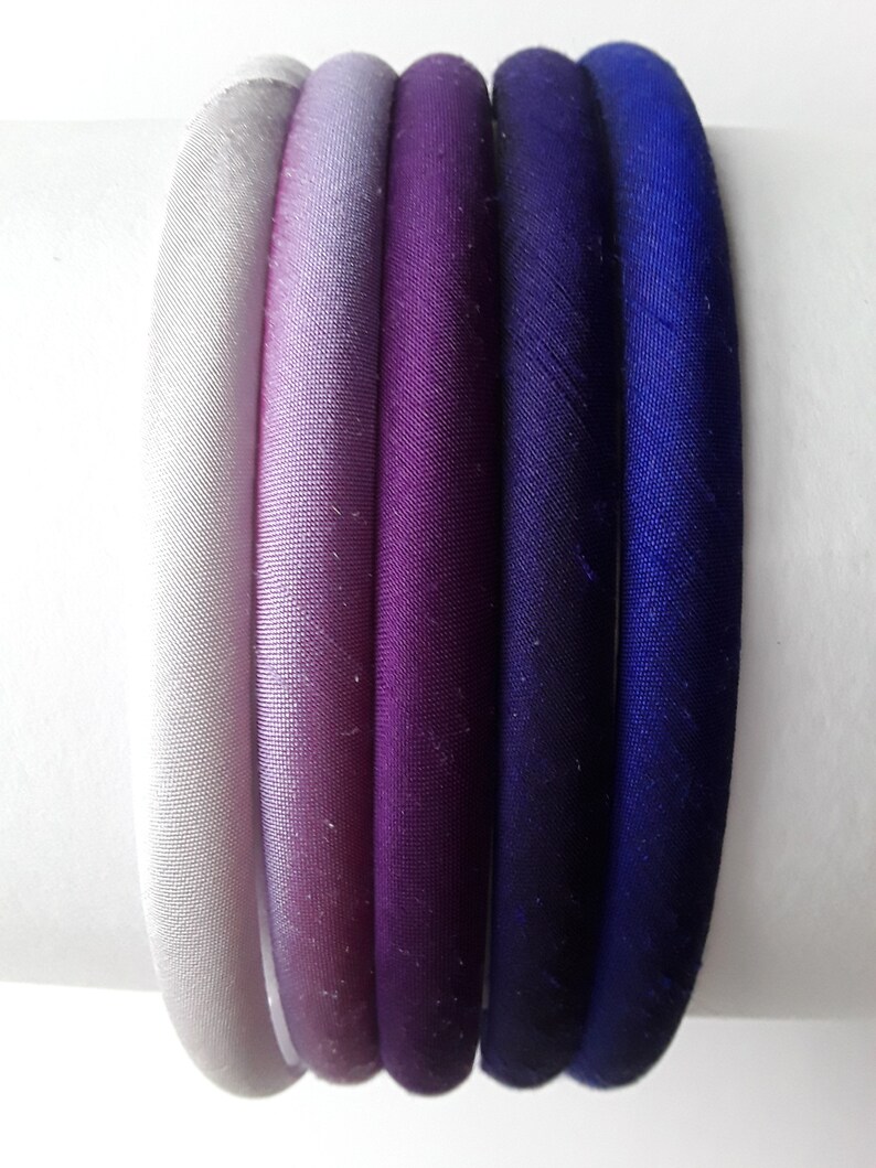 May include: Set of six hair ties in a gradient of colors from white to purple to blue. The hair ties are made of a soft, silky fabric.