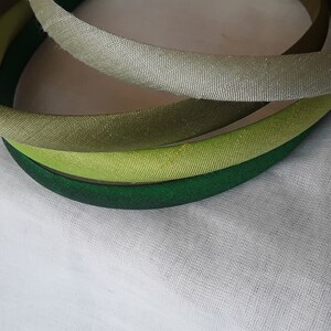 May include: Four fabric headbands in shades of green, light green, and gray. The headbands are stacked on top of each other.