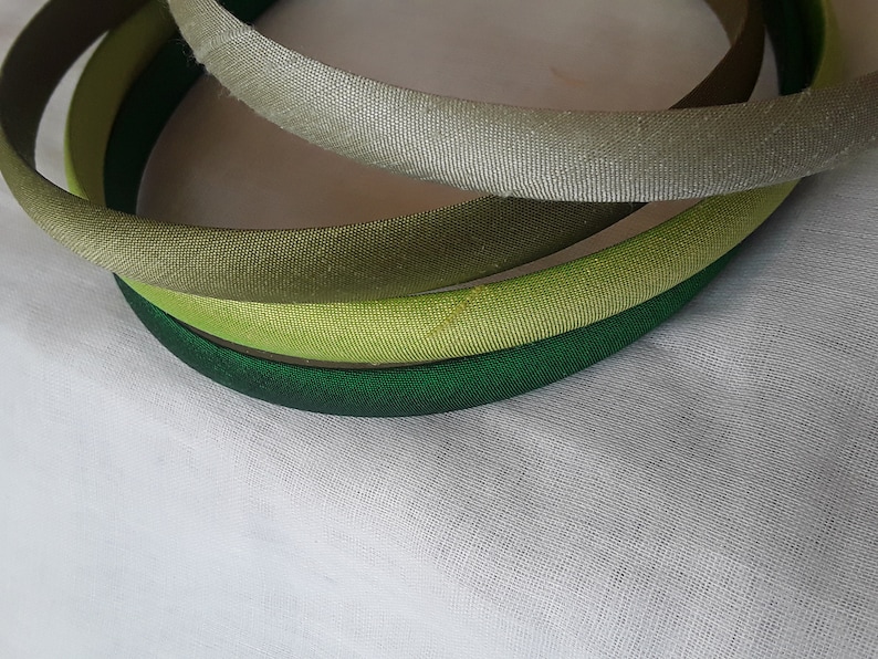 May include: Four fabric headbands in shades of green, light green, and gray. The headbands are stacked on top of each other.