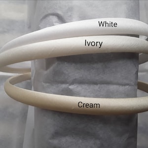 May include: Three satin headbands in different shades of white: white, ivory, and cream.