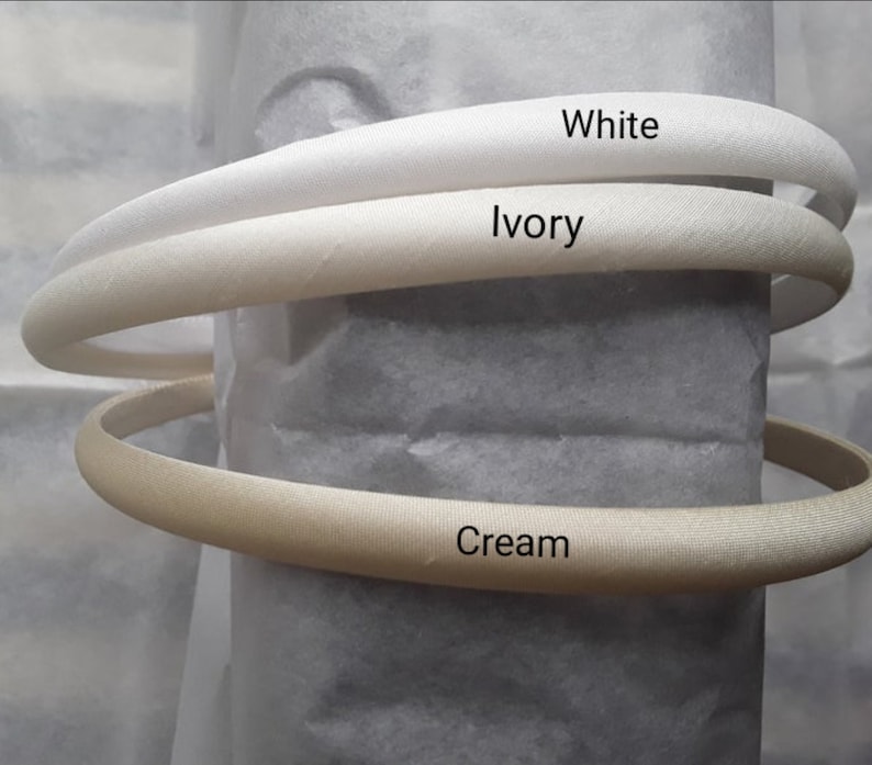 May include: Three satin headbands in different shades of white: white, ivory, and cream.