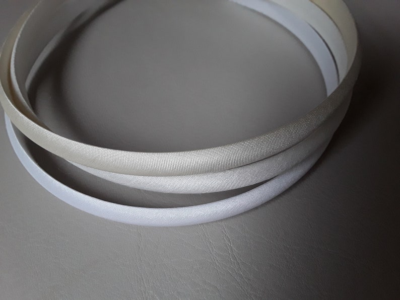 May include: Three white satin headbands, stacked on top of each other. The headbands are all the same size and shape, and they are made of a soft, silky material.