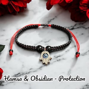 Puede incluir: Pulsera de cuerda negra y roja con un dije de mano de Hamsa plateado con un ojo turco azul. La pulsera también tiene dos cuentas de obsidiana negra. El texto "Hamsa & Obsidian - Protección" está en la parte inferior de la imagen.