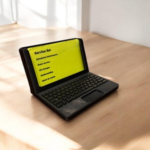 A 3d printed business card holder in the design of a laptop computer, holding a green business card, sitting on a wooden desk.