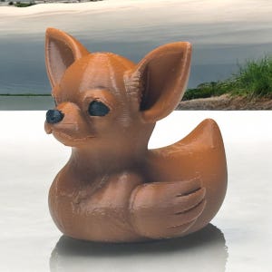 Könnte beinhalten: Eine braune Gummiente in Form eines Chihuahuas. Die Ente hat schwarze Augen und eine schwarze Nase.