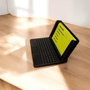 A 3d printed business card holder in the design of a laptop computer, holding a green business card, sitting on a wooden desk.