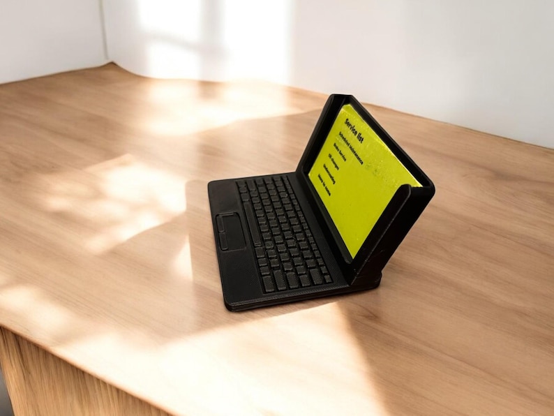 A 3d printed business card holder in the design of a laptop computer, holding a green business card, sitting on a wooden desk.