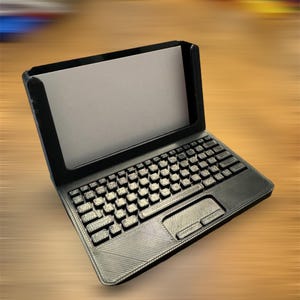 A 3d printed business card holder in the design of a laptop computer, holding a white business card, sitting on a wooden desk.
