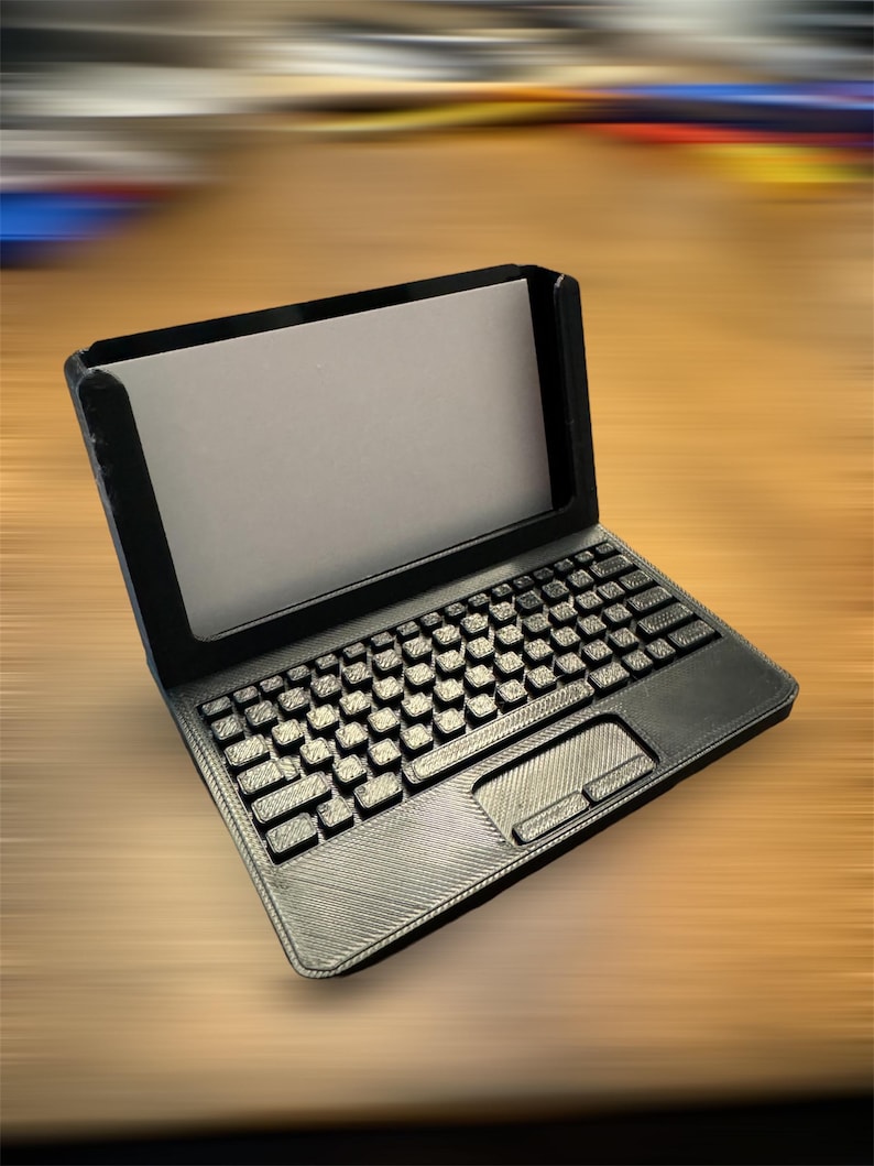A 3d printed business card holder in the design of a laptop computer, holding a white business card, sitting on a wooden desk.