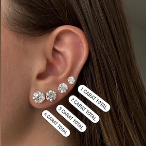Puede incluir: Cuatro pares de pendientes de diamantes redondos y transparentes de diferentes tamaños. Los pendientes se muestran en la oreja de una persona. El texto debajo de los pendientes dice "1 quilate total", "2 quilates total", "3 quilates total" y "4 quilates total".