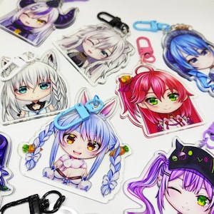 Könnte beinhalten: Eine Sammlung von bunten Anime-Charakter-Schlüsselanhängern mit verschiedenen Designs. Jeder Schlüsselanhänger zeigt einen anderen Charakter mit einzigartigen Haarfarben, Outfits und Accessoires. Die Schlüsselanhänger sind aus klarem Acryl gefertigt und haben Metallringe zum Anbringen an Schlüsseln oder Taschen.