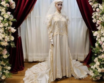 Könnte beinhalten: Ein weißes Brautkleid mit langem Schleier und Spitzendetails. Das Kleid hat einen hohen Ausschnitt und lange Ärmel. Das Kleid wird auf einer Schaufensterpuppe in einem Studio ausgestellt.